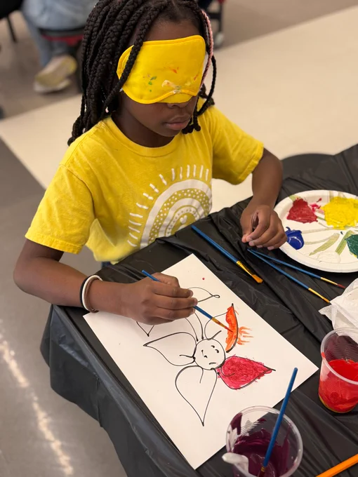 A workshop attendee at West Lafayette Intermediate School is seen wearing a blindfold as she paints a flower.