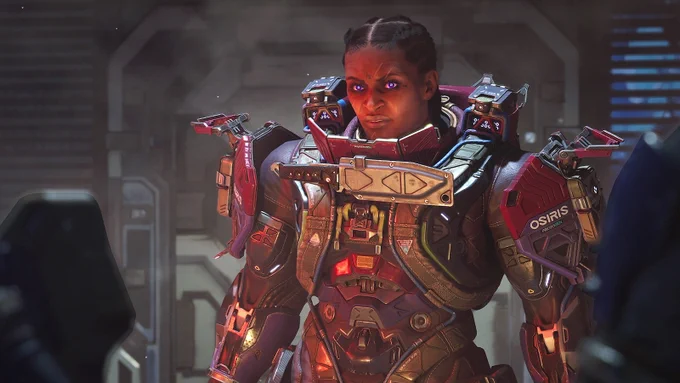 A darker skinned female-looking character in bulky red space armour with glowing eyes stands facing down two approaching people. If they want to fight her, it looks like they've got a serious battle on their hands.