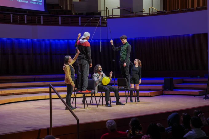 A performer on stage with different audience members performing an illusion