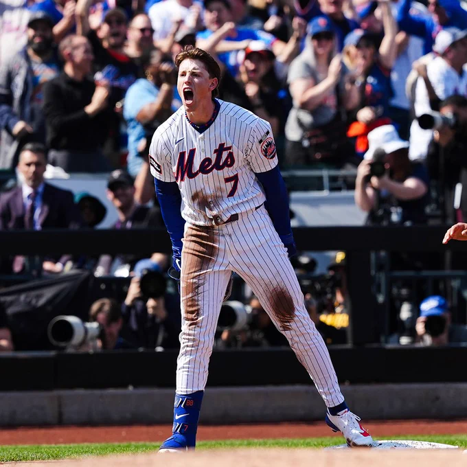 Brett Baty yells after his bases-clearing triple. He wears a dirtied white Mets uniform with orange and blue lettering.