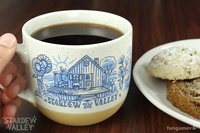A photo of someone holding the Farm Life mug, a large retro-looking round mug with a beige bottom and an off-white top. It's decorated with a pale blue illustration of a farmhouse with the words Stardew Valley below it.