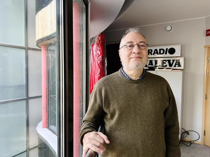 Professor Marcos Katz stands indoors near a large window, holding a pen. Behind them, there is a sign that reads "Radio Kaleva".