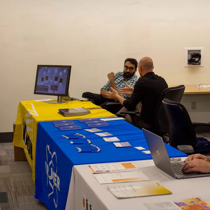 Two representatives from Nikon talk with one another at a booth. 
