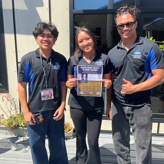 Three people stand together. One person holds a flyer.