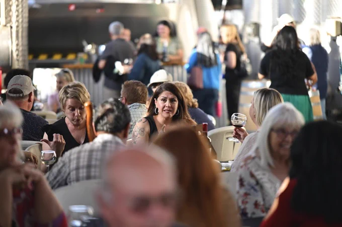 This image shows a bustling winery tasting room with people seated at tables engaged in conversation, enjoying wine. The setting appears lively and social.