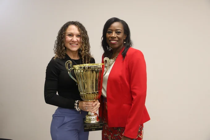 two women dressed in business casual, holding a large trophy
