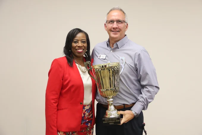 Man and woman dressed in business casual holding a large gold trophy