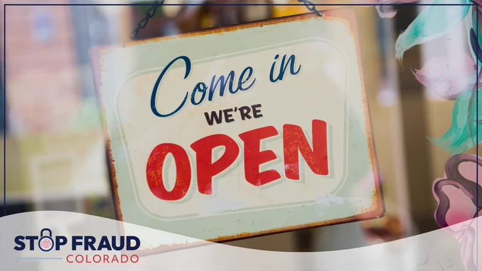 Aged and colorful 'Come in We're Open' sign hanging on a glass door, with the logo 'Stop Fraud Colorado' in the corner.
