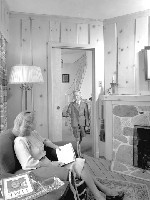 black and white photograph from 1946 of a boy walking through a door into a reading room looking at his mother seated in a comfy chair.