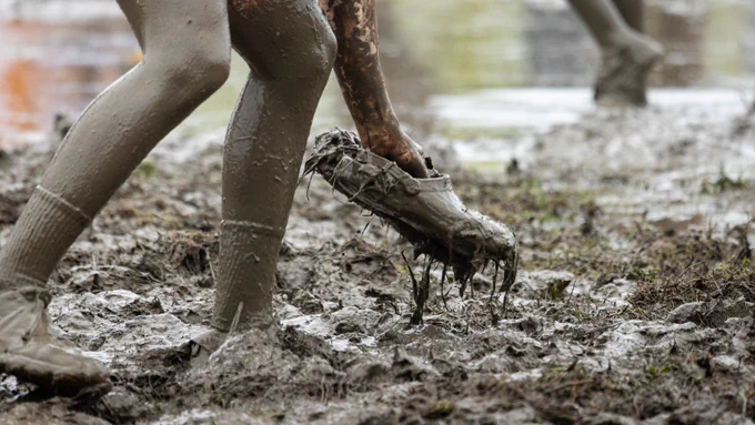 Someone picking up a shoe covered in mud.