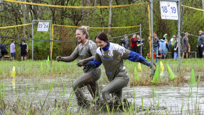 Two women holding hands while crossing a muddy volleyball court.