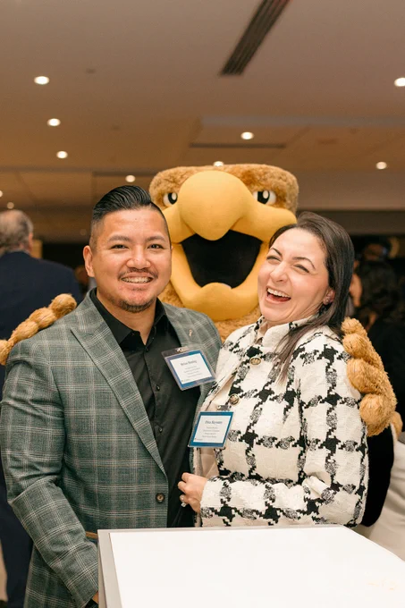Two people are smiling and standing with the Humber Polytechnic mascot.
