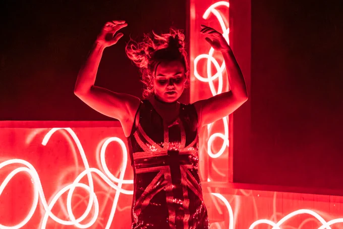 A young woman dances with her hands in the air, lit by red neon lights