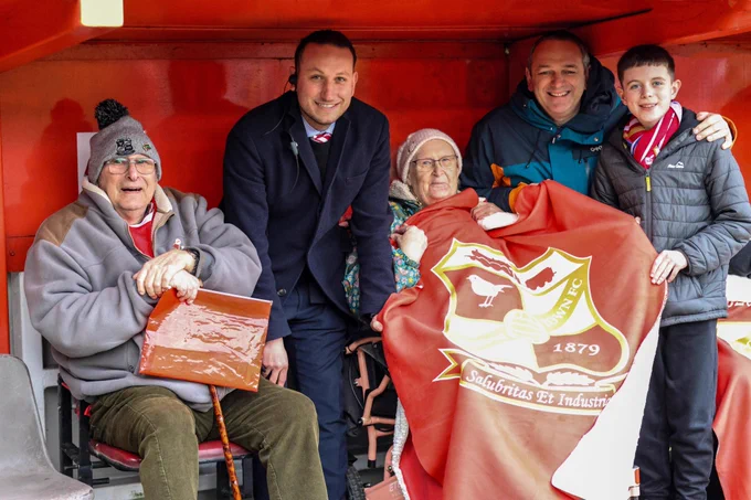 A group of people sitting in a wheelchair user viewing area, holding a blanket.