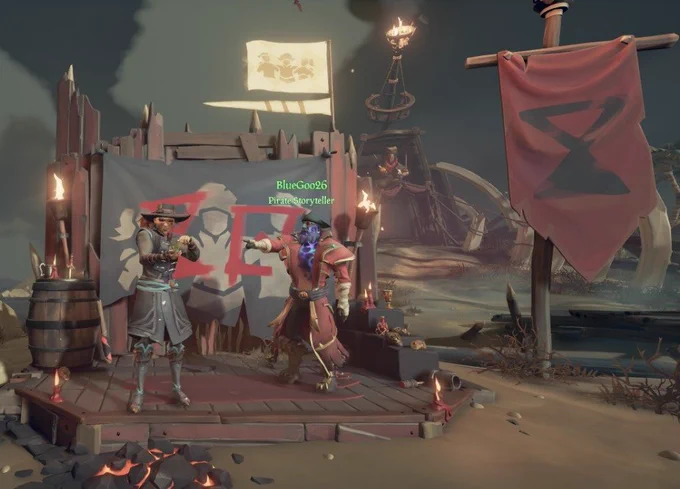 Two sea of theives pirates stood in front of the season 18 community weekend photo wall at reapers hideout. Bluegoo26  is pointing at Rage Pixie who is using the touching grass emote .
