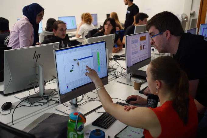 A group of people working at computer workstations in a classroom, with one person pointing and asking a question about using a data visualisation software called WellCAD. Photo credit: Erwan Le Ber.