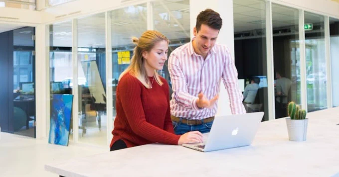 Two colleagues collaborating with a laptop in a modern office