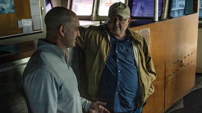 Two men speak inside the ship’s bridge, discussing vessel operations during a guided tour.