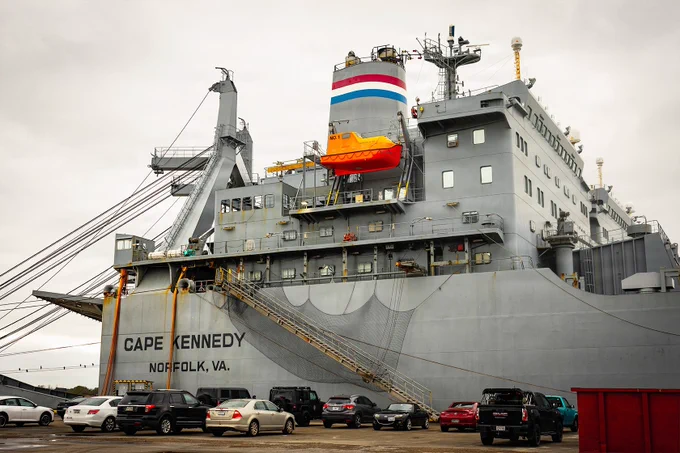 Military Sealift Command ship Cape Kennedy docked in New Orleans, with vehicles parked along the pier.