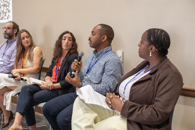 A group shot of participants in the panel on Perspectives on the Future of Learning Technologies during the National AI Literacy Day @ UF conference. The entire group is listening attentively while a man wearing a blue and white checkered shirt speaks into a microphone. 