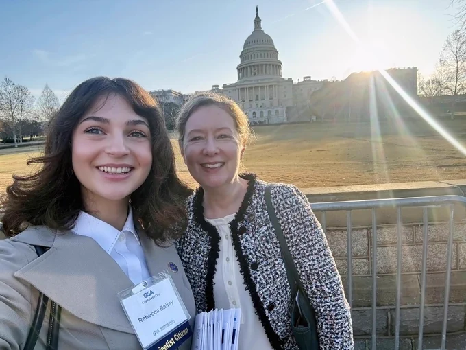 Two people smiling in front of the U.S. Capitol building with the sun shining in the sky.