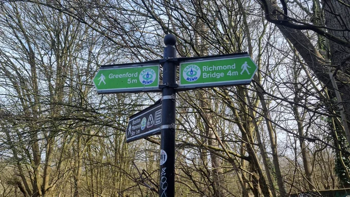 An ornate Capital Ring finger post in a wooded area close to Boston Manor.  To the right it says Richmond Bridge 4m and to the left Greenford 5m.