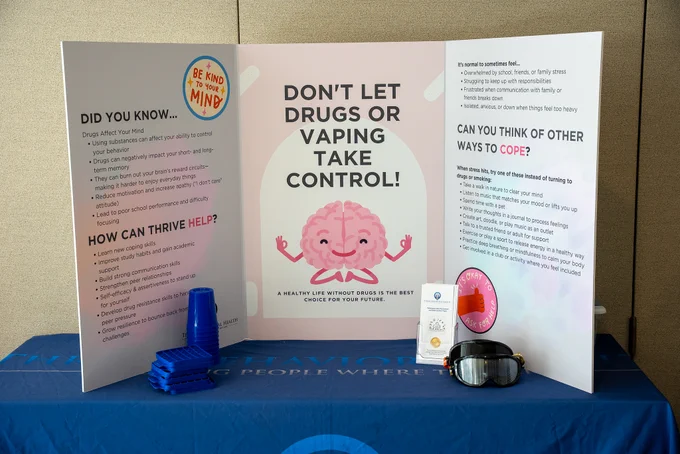 A mental health awareness display with a pink brain cartoon and messages urging to avoid drugs and vaping, offering coping strategies and support resources at the Mind Over Matters event