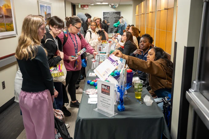 Students lined up at a table in a hallway, engaging with representatives handing out informational materials and promotional items during the Mind Over Matters event