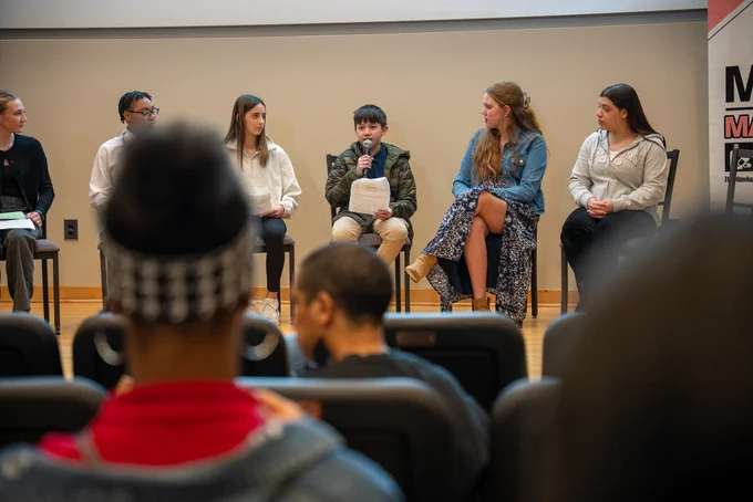 A group of five students seated on stage in a panel discussion, with an audience watching attentively in the foreground at the Mind Over Matters event