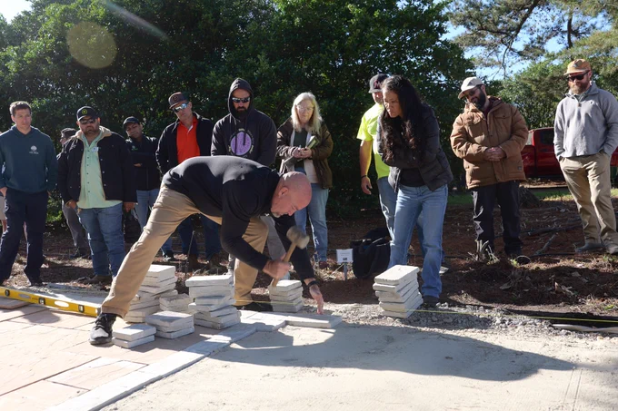 A man uses a rubber mallet to install pavers. 