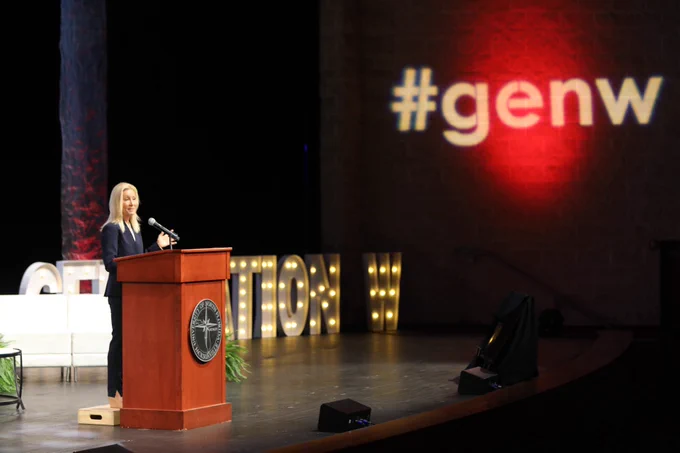 Mayor Deegan, speaking behind a podium with the words #genw in the background