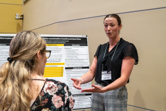Amelia Wiercioch, standing next to her poster presentation, engages in conversation with a person in front of her.