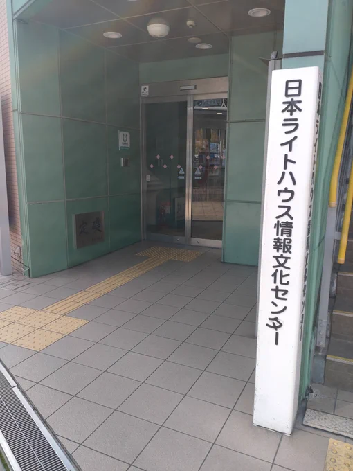当館入口の写真です。
点字ブロックの先に自動扉があります。
手前に日本ライトハウス情報文化センターと書かれた
白い四角柱の看板が立っています。