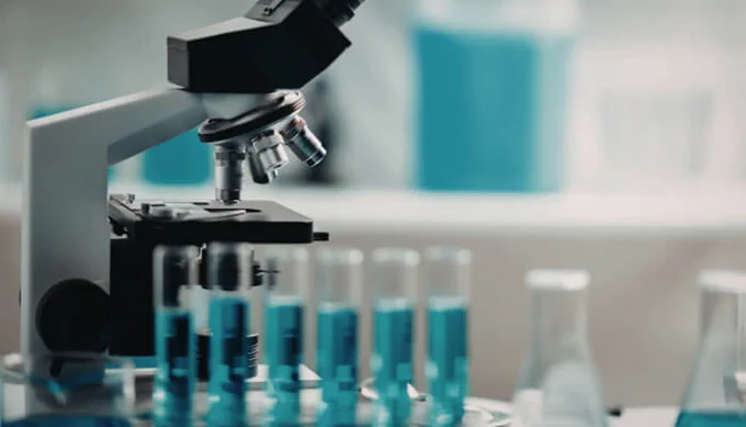 Close-up view of a laboratory microscope with test tubes filled with blue liquid, symbolizing the importance of quality lab supplies in research and experiments.
