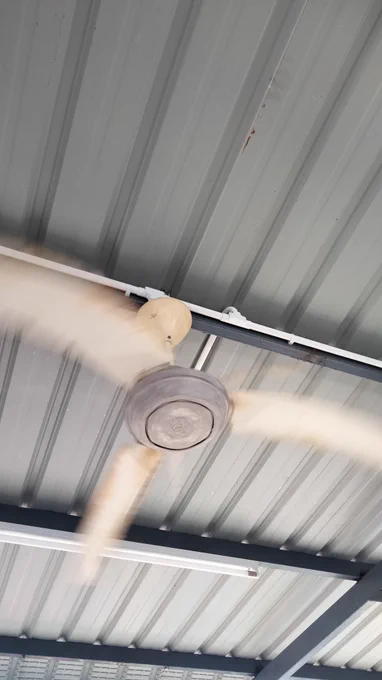 Underside of a metal deck roof in grey colour with a rotating ceiling fan hanging under it