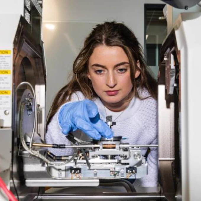 Scientist wearing blue gloves adjusting components inside a high-tech laboratory instrument.