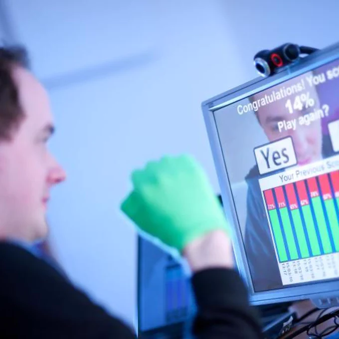 Person wearing a green glove interacts with a screen showing a 14% score and options to play again with Yes or No buttons.
