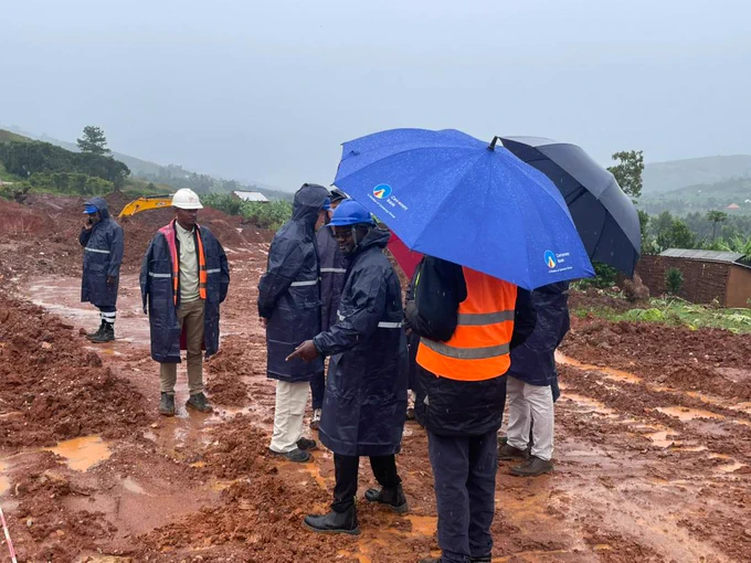Participants standing on muddy group at a mining site visit, wearing hi-vis, helmets and holding umbrellas. 