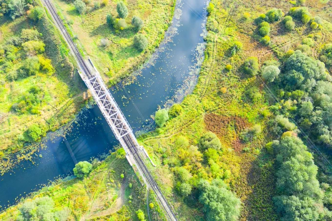 Image is an aerial photograph of a bridge over a river. Trees stand on either side of the river.