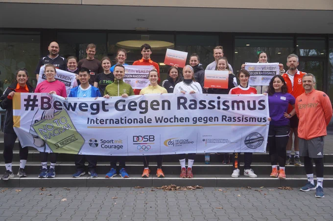 Eine Gruppe Läufer*innen hält ein Banner hoch. Auf dem Banner steht: #Bewegt gegen Rasissmus.