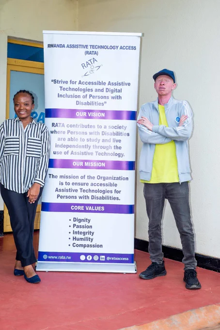 A woman in a striped shirt and a man with albinism in a grey tracksuit posing on either side of a RATA banner.
