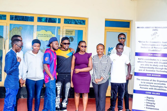A group of nine young adults posing together outside next to a Rwanda Assistive Technology Access (RATA) informational banner.
