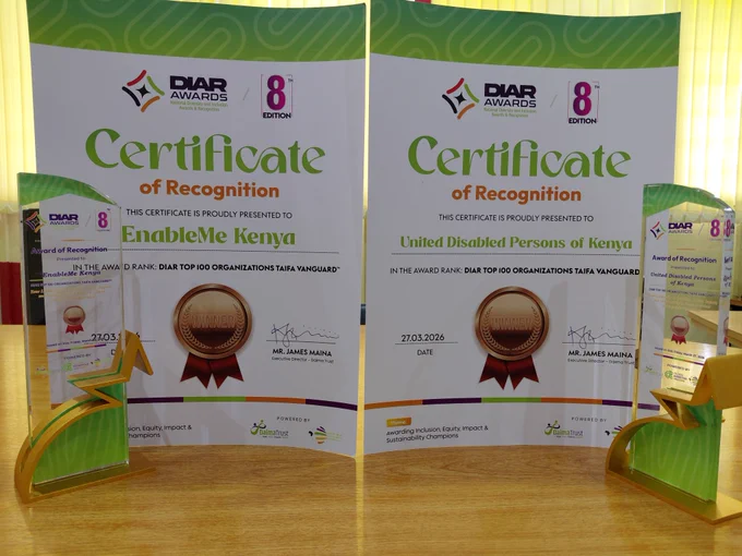 Two DIAR Awards 8th Edition certificates of recognition are displayed side by side on a table, awarded to EnableMe Kenya and the United Disabled Persons of Kenya under the DIAR Top 100 Organizations Taifa Vanguard category.

In front of each certificate is a glass award trophy with a star design. The certificates feature a “Winner” seal, the date 27.03.2026, and signatures, with DIAR Awards and Daima Trust branding visible.