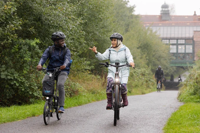 Two people cycle along a path.