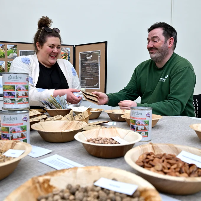 A man and lady sat behind a table with bowls of seeds.
