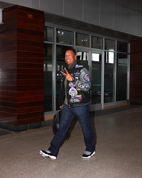 Salvador Perez walks in wearing a jacket with multiple patches showing his accolades over his career. (Photo by Sydney Schneider/Major League Baseball)