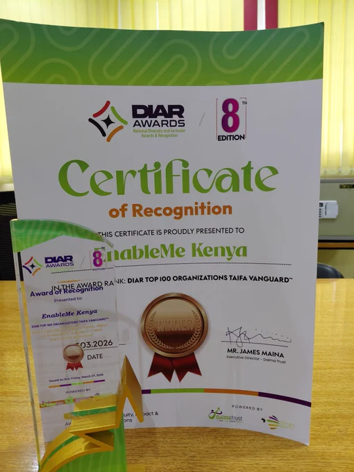 A Certificate of Recognition and a glass trophy awarded to EnableMe Kenya at the 8th Edition of the DIAR Awards (National Diversity and Inclusion Awards & Recognition).

The certificate features a green and white wavy design and states that EnableMe Kenya has been ranked in the "DIAR TOP 100 ORGANIZATIONS TAIFA VANGUARD." It is signed by Mr. James Maina, Executive Director of Daima Trust, and dated March 2026.

In the foreground, a tall, clear acrylic trophy with green and gold accents sits on a wooden table, mirroring the award details on the certificate. A gold "Winner" seal with a red ribbon is prominently displayed in the center of the certificate.