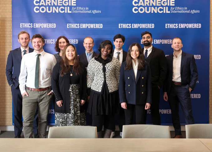 Group of nine professionals posing in front of a blue Carnegie Council backdrop promoting ethics in international affairs.