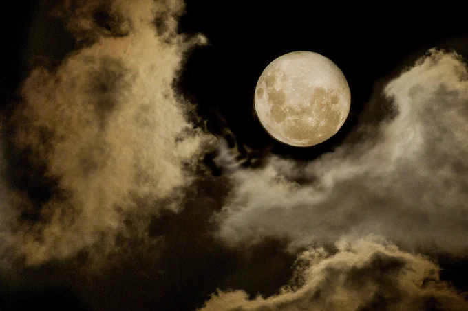 Moon shines through dark clouds and lights up the dark sky