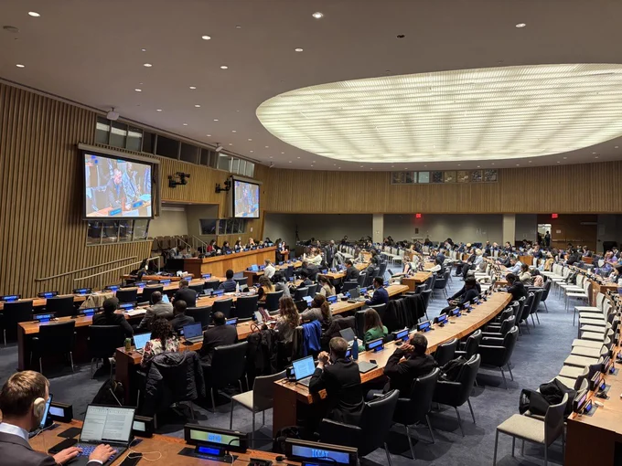 Picture on the left is showing a wide view of a large United Nations conference room during the third session of the BBNJ Agreement Preparatory Commission meeting. Delegates sit at long curved desks with microphones and laptops, while two large screens display speakers at the front of the room. The chamber is brightly lit with a circular ceiling light feature.

Picture on the right is showing Delegates seated in a United Nations meeting room participating in the third session of the BBNJ Agreement Preparatory Commission meeting. Two large screens show a speaker addressing the room from the podium. Nameplates for countries such as Lithuania, Luxembourg, and Madagascar are visible in the foreground.